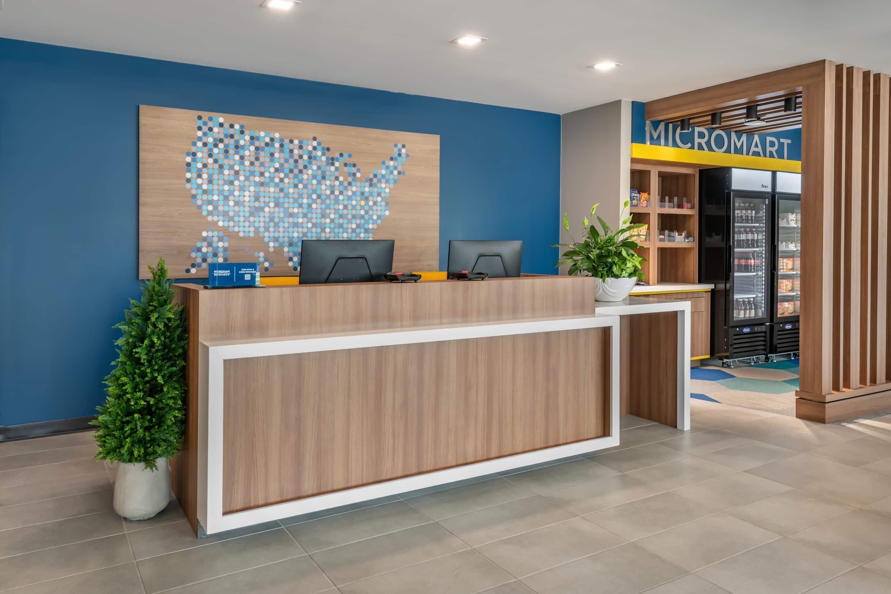 A reception desk with two computer monitors, a plant, and a wall art of a blue dot map.