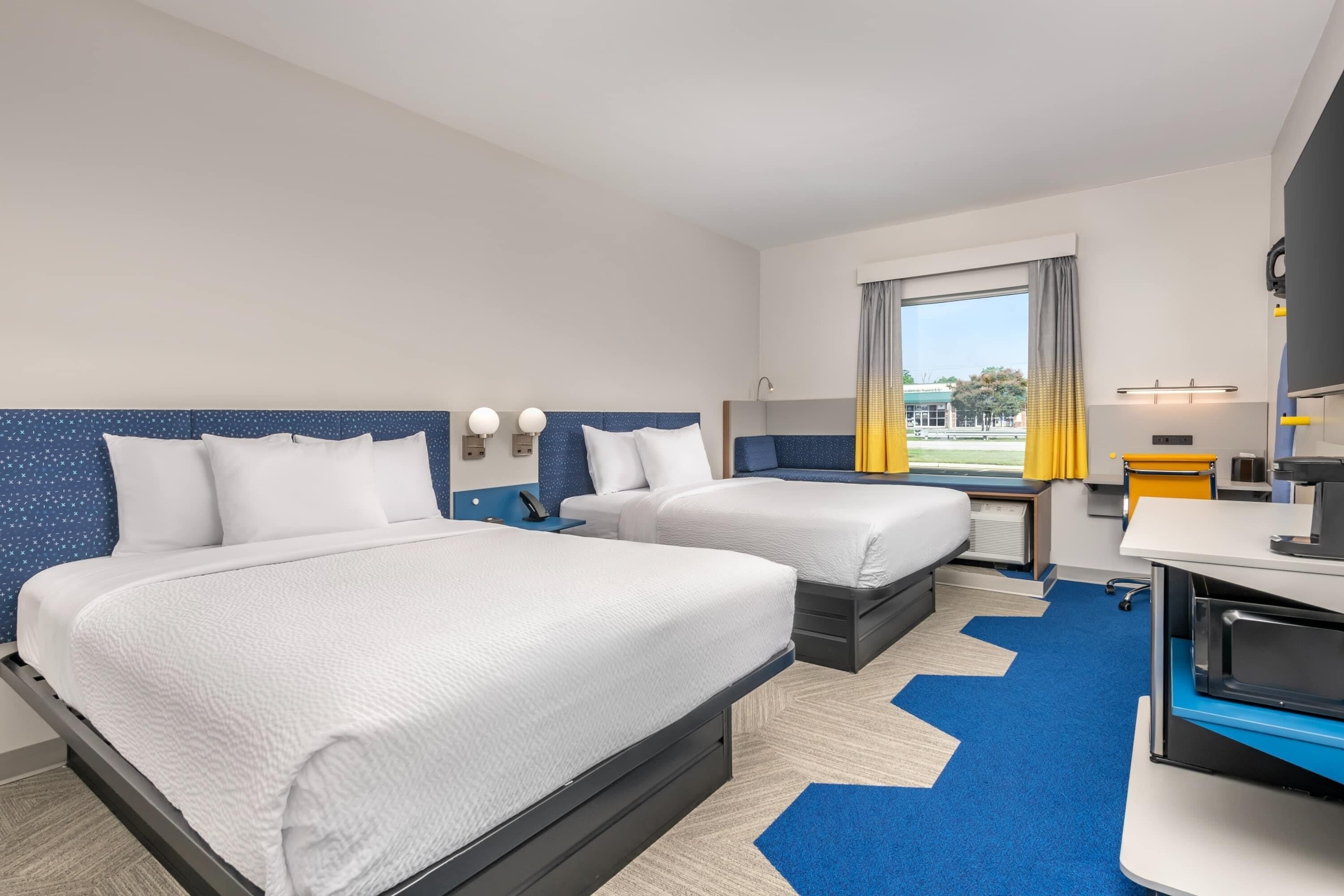 A hotel room with two beds, a desk, a chair, a TV, and a window with curtains.