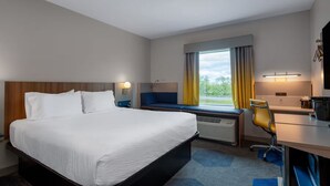 Une chambre d’hôtel avec un lit, un bureau, une chaise, une fenêtre avec des rideaux et une vue sur l’extérieur.