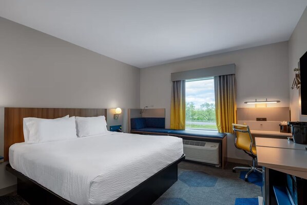 A hotel room with a bed, a desk, a chair, a window with curtains, and a view of the outdoors. - Microtel Inn & Suites By Wyndham Danville Va (Danville)