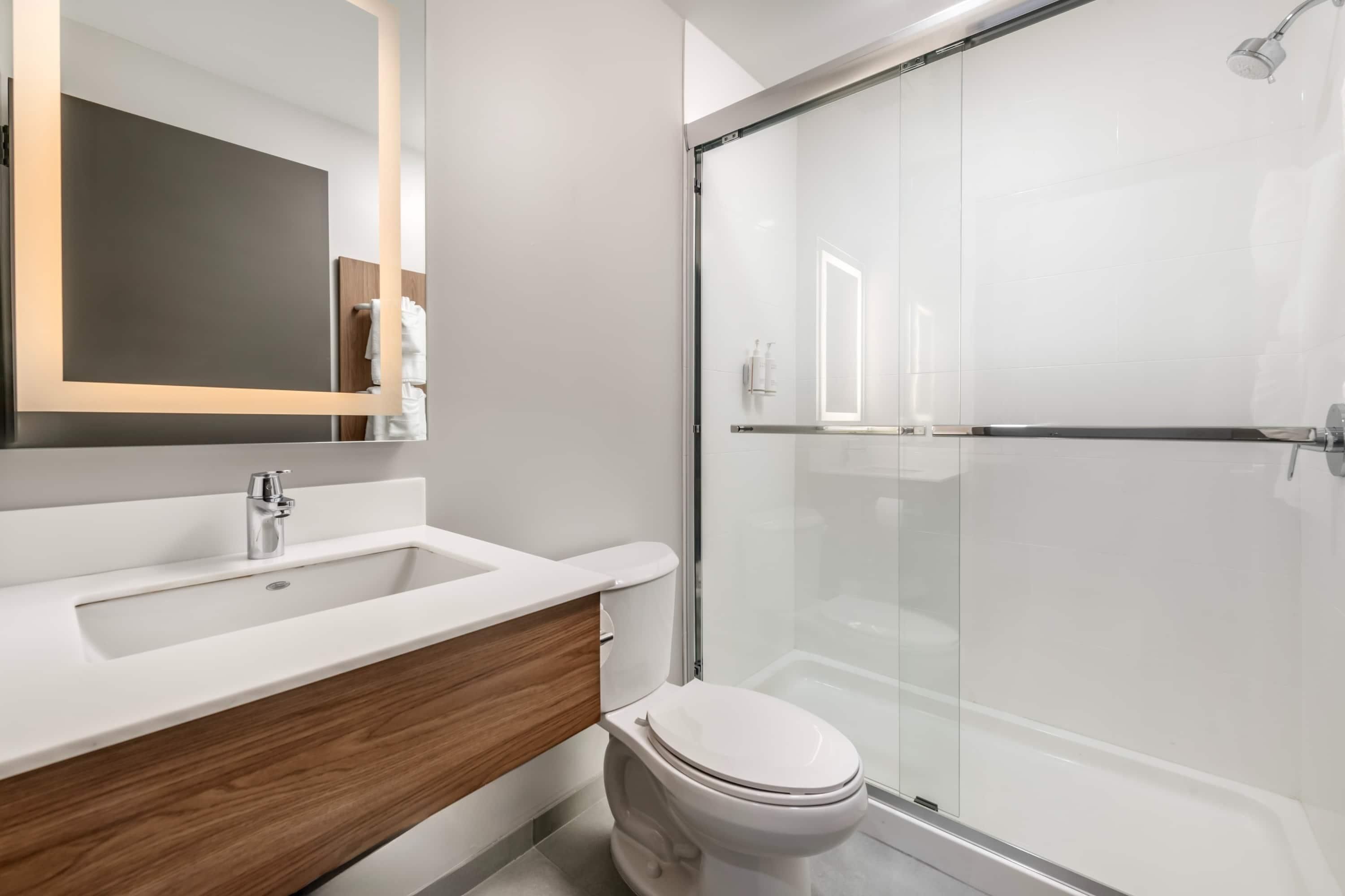 Un baño moderno con cabina de ducha de vidrio, un lavabo blanco y un mueble de tocador de madera.