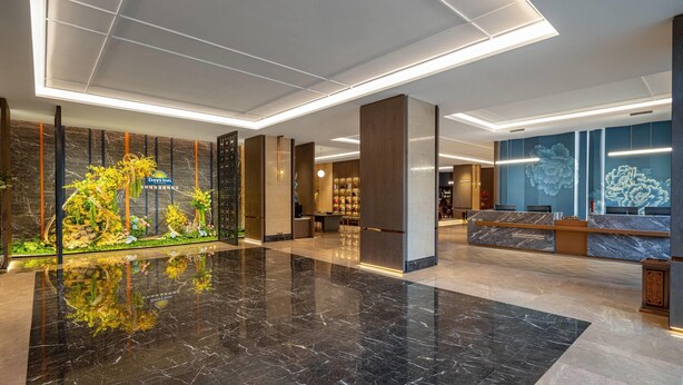 Een hotel lobby met een receptiebalie, een decoratieve plantenpresentatie en een modern plafondontwerp.