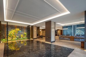 A hotel lobby with a reception desk, a decorative plant display, and a modern ceiling design. - Days Inn By Wyndham Kunming Changshui Airport (Kunming)