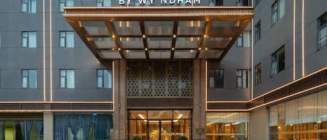 A hotel entrance with a glass facade, a sign above the entrance, and a covered area with lights.