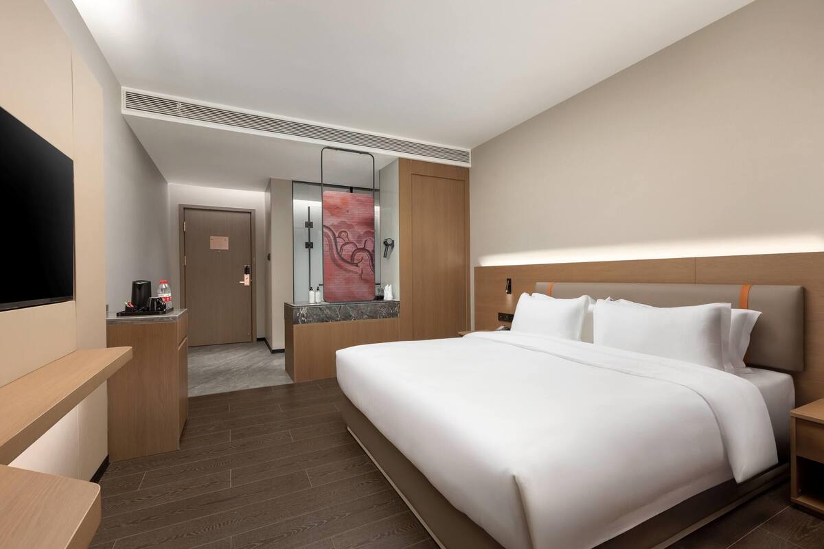 Een hotelkamer met een groot bed, een bureau, een televisie en een badkamer met spiegel en handdoekrek.