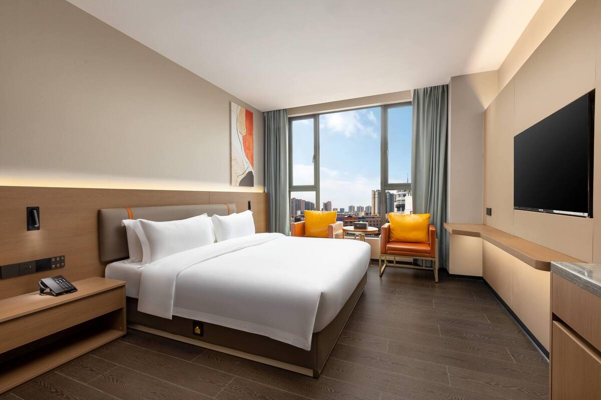 Hotelkamer met een groot bed, een bureau met telefoon, een televisie, een stoel en uitzicht op de stad.