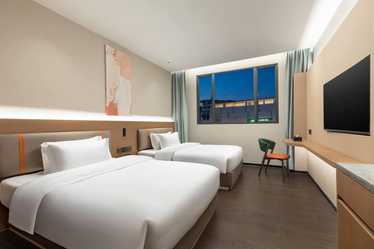 Een hotelkamer met twee bedden, een bureau, een stoel, een televisie en een raam met uitzicht op de stad.