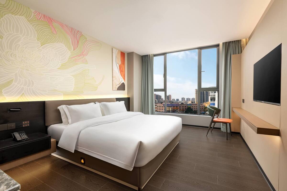 Een hotelkamer met een groot bed, een bureau met stoel, een televisie en uitzicht op de stad.
