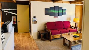 Un salon avec un canapé rouge, une table basse en bois et une œuvre d’art accrochée au mur.