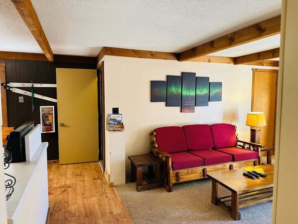 Una sala de estar con un sofá rojo, una mesa de centro de madera y una obra de arte colgada en la pared.