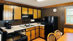 Une cuisine compacte avec des meubles en bois, un réfrigérateur noir, un four à micro-ondes et une table à manger avec des chaises.