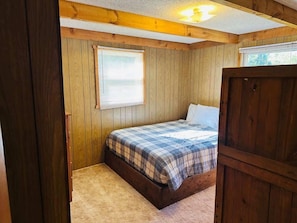 A bedroom with a wooden bunk bed, a window with blinds, and a door.