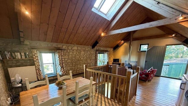 Un interior de madera con comedor, paredes de piedra y vista a través de una ventana.