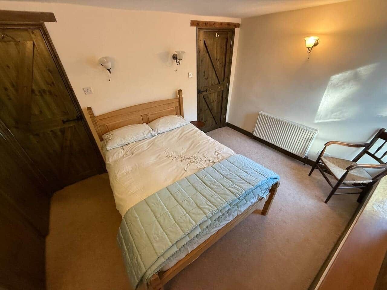 A bedroom with a wooden bed, a chair, a radiator, and a door.