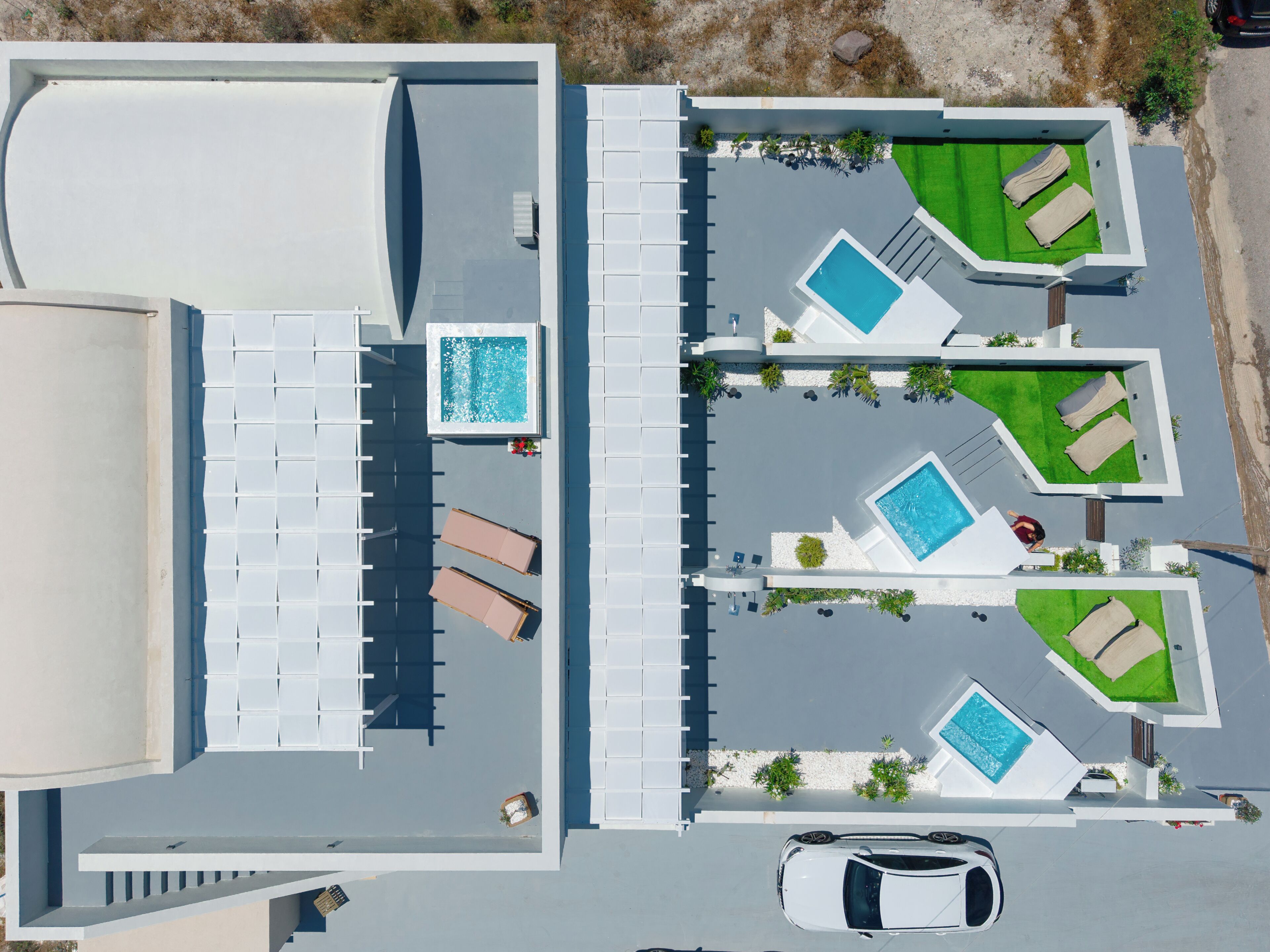 Vue aérienne d’un hôtel moderne doté de plusieurs piscines, de chaises longues et d’un parking.