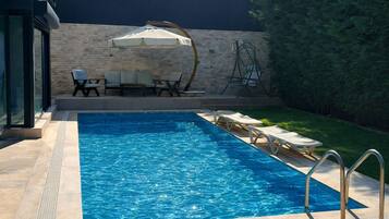 Ein Swimmingpool mit Liegestühlen und Sonnenschirm, umgeben von einer Steinmauer und viel Grün.