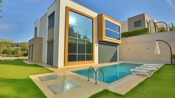 A modern two-story house with a swimming pool, large windows, and a well-maintained lawn.