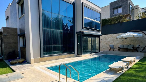 Uma casa moderna com piscina, um pátio com espreguiçadeiras e uma parede de pedra.