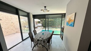 Uma área de refeições com mesa e cadeiras, grandes portas de vidro deslizantes, um lustre e um quadro na parede.