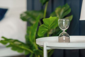 Eine klare Sanduhr steht auf einem weißen Tisch, im Hintergrund ist eine grüne Pflanze zu sehen.