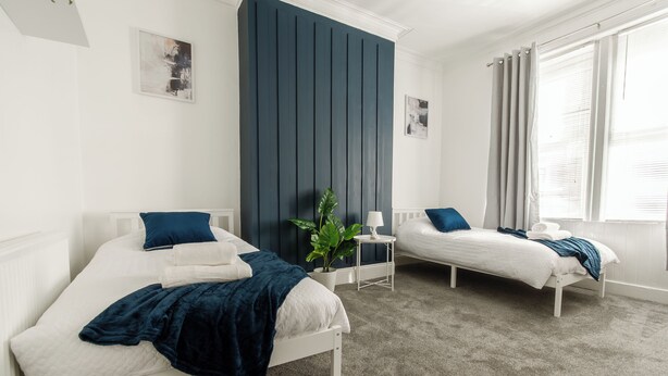 Een slaapkamer met twee bedden, een donkere accentmuur, een klein tafeltje en een raam met gordijnen.