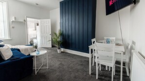 Een moderne woonkamer met een donkerblauwe accentmuur, een witte bank, een klein rond tafeltje en een wit eetgedeelte.