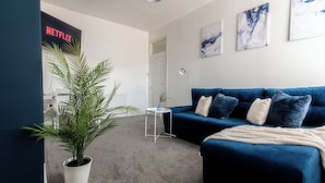 Een moderne woonkamer met een blauwe bank, een witte potplant, een klein bijzettafeltje en een Netflix-bordje.