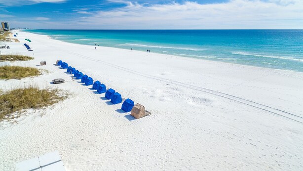 A beach with white sand, a clear blue ocean, and a row of blue tents. - Family Fun Condo Near Private Beach Silver Dunes 48 (Destin)