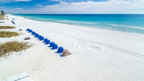 A beach with white sand, a clear blue ocean, and a row of blue tents. - Family Fun Condo Near Private Beach Silver Dunes 48 (Destin)