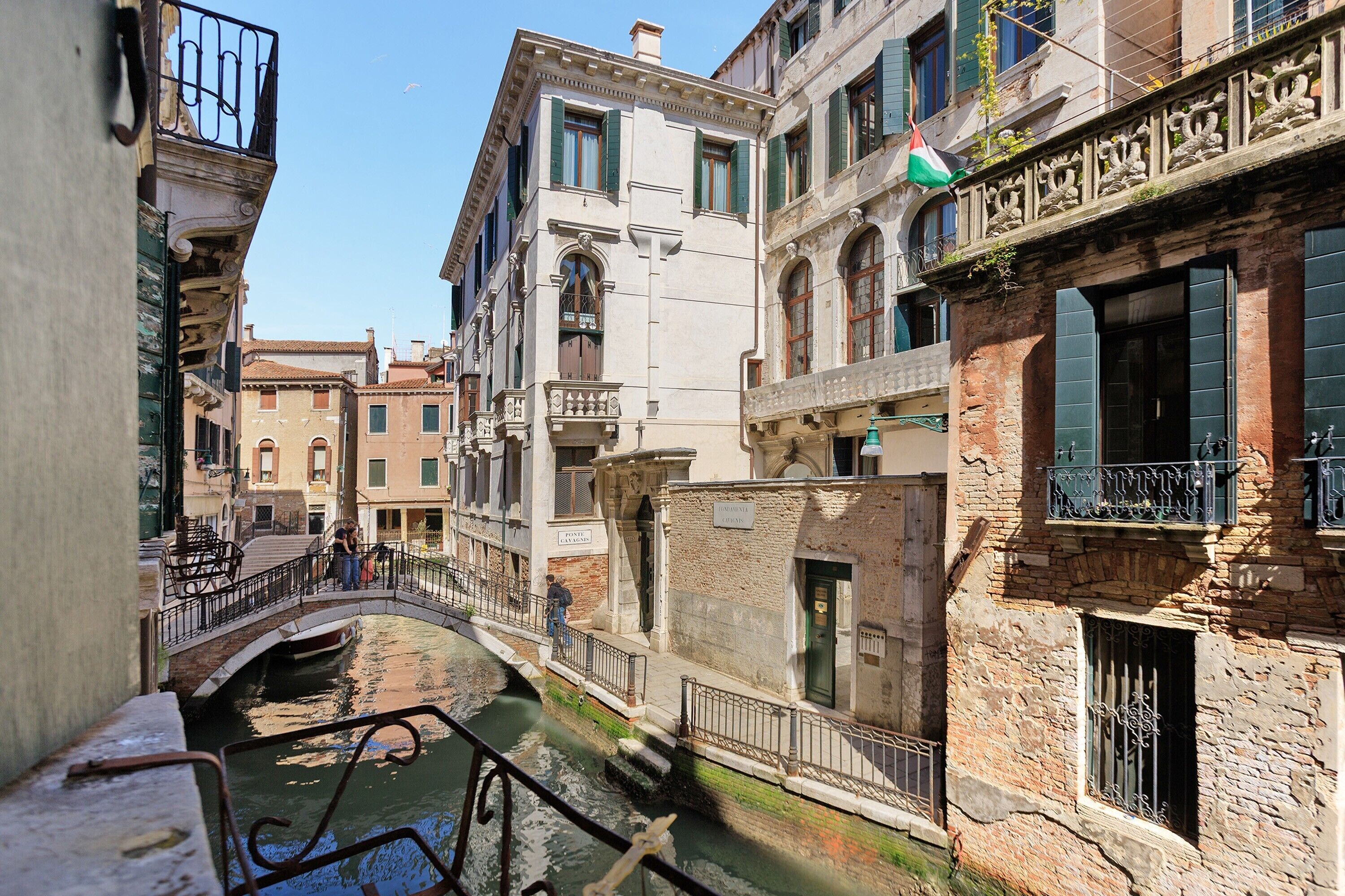 A narrow canal with buildings on either side, a bridge, and a flag.