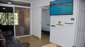 A living room with a brown leather sofa, a wooden coffee table, a TV mounted on the wall, and a sliding glass door leading to a balcony. - Great magic, 5 minutes from the sea! Ideal apartment for families of 4 people. (cancun)