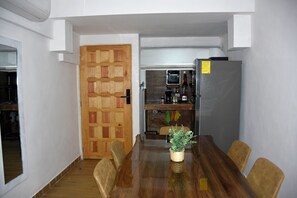 A dining area with a wooden table, chairs, a potted plant, a kitchen in the background, and a wooden door. - Great magic, 5 minutes from the sea! Ideal apartment for families of 4 people. (cancun)