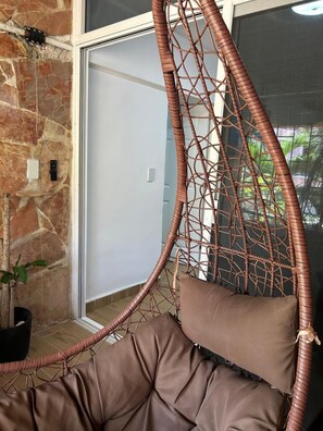 A wicker hanging chair with cushions, a stone wall, a door, and a potted plant. - Great magic, 5 minutes from the sea! Ideal apartment for families of 4 people. (cancun)