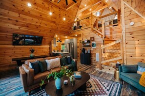 A wooden cabin interior with a living room, kitchen, and a staircase leading to an upper level. - Back Yard Cliff View | Elevated Cabin | Hot Tub | Fire pit (Lee County)