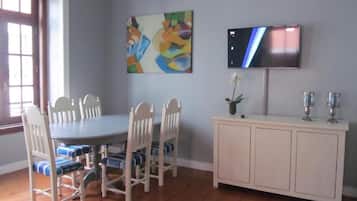 A dining area with a round table, six chairs, a cabinet, a TV, and a painting on the wall.