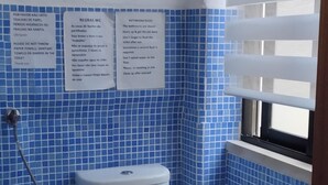 A small bathroom with a toilet, a trash bin, and two signs with bathroom rules in a foreign language. - Casa Azul Hostel (Sintra)