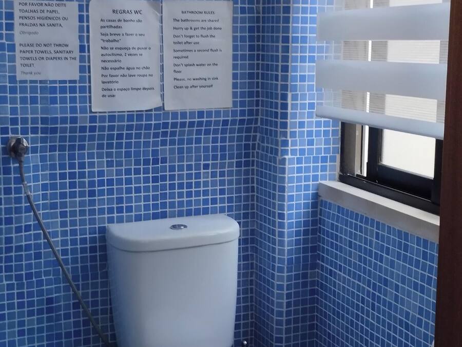 Une petite salle de bain équipée de toilettes, d’une poubelle et de deux panneaux indiquant les règles d’utilisation, rédigés dans une langue étrangère.