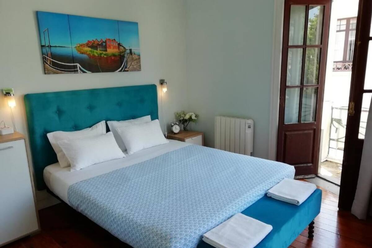 Un dormitorio con cama, mesita de noche, cuadro, ventana y puerta.