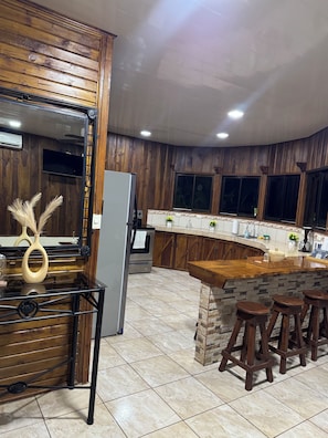 A kitchen with wooden cabinets, a built-in oven, a refrigerator, a bar area with stools, and a stone accent wall.