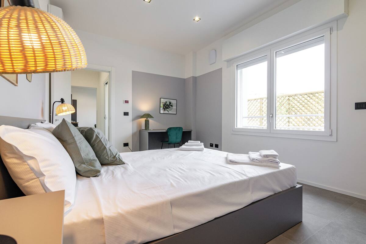 A modern bedroom with a large bed, a desk, and a window.