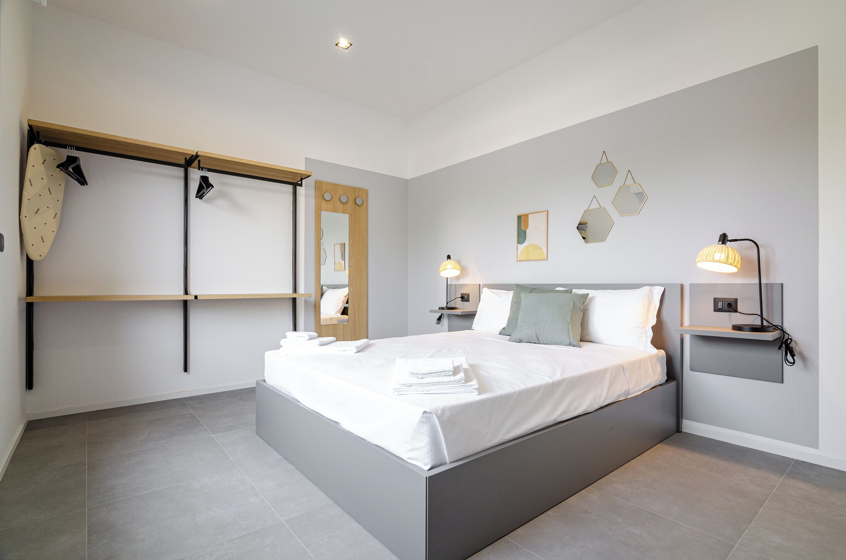 A modern bedroom with a bed, bedside tables, a mirror, and wall-mounted lights.