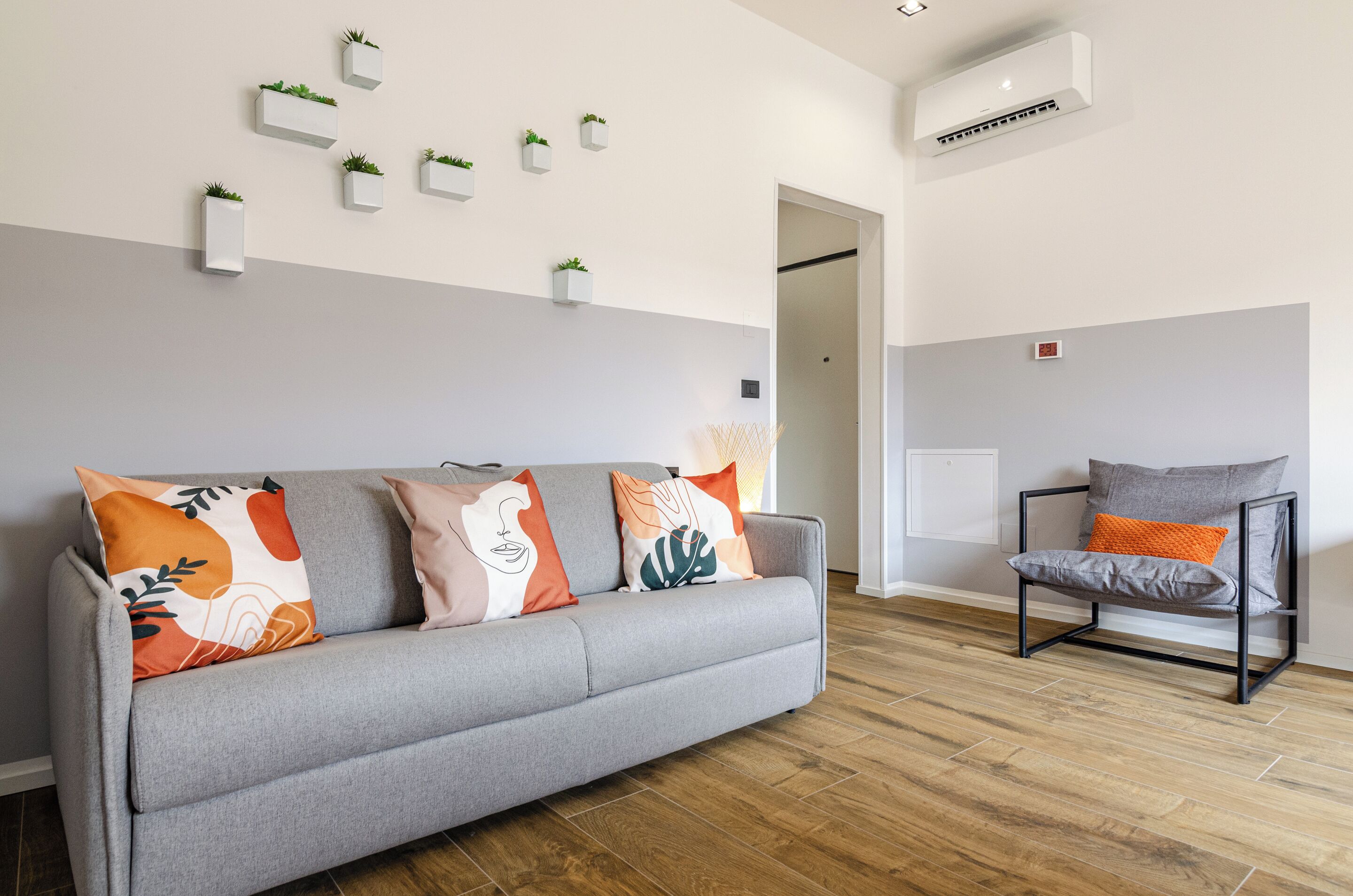 A modern living room with a grey sofa, a grey armchair, and a wall-mounted air conditioner.