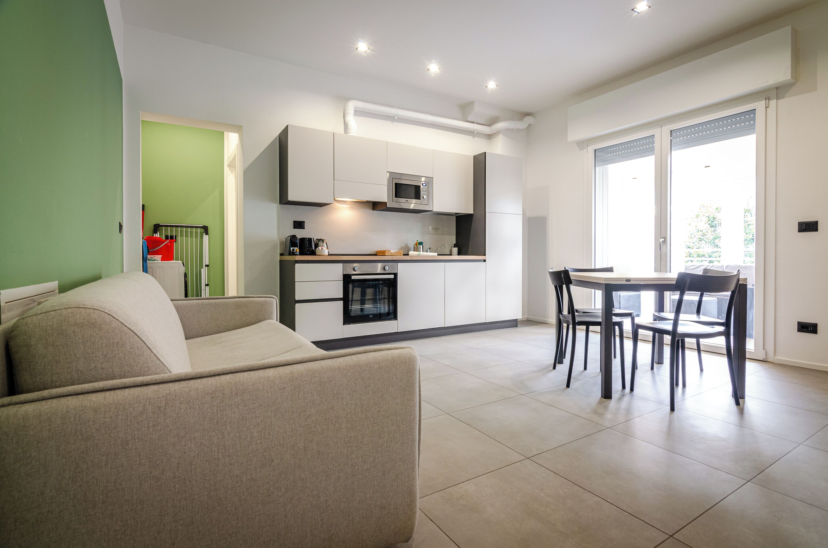 A modern kitchen with a dining area, a sofa, and a view of the outdoors.