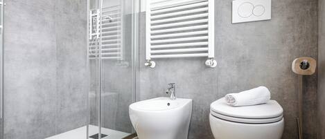 A modern bathroom with a glass-enclosed shower, a bidet, and a toilet.