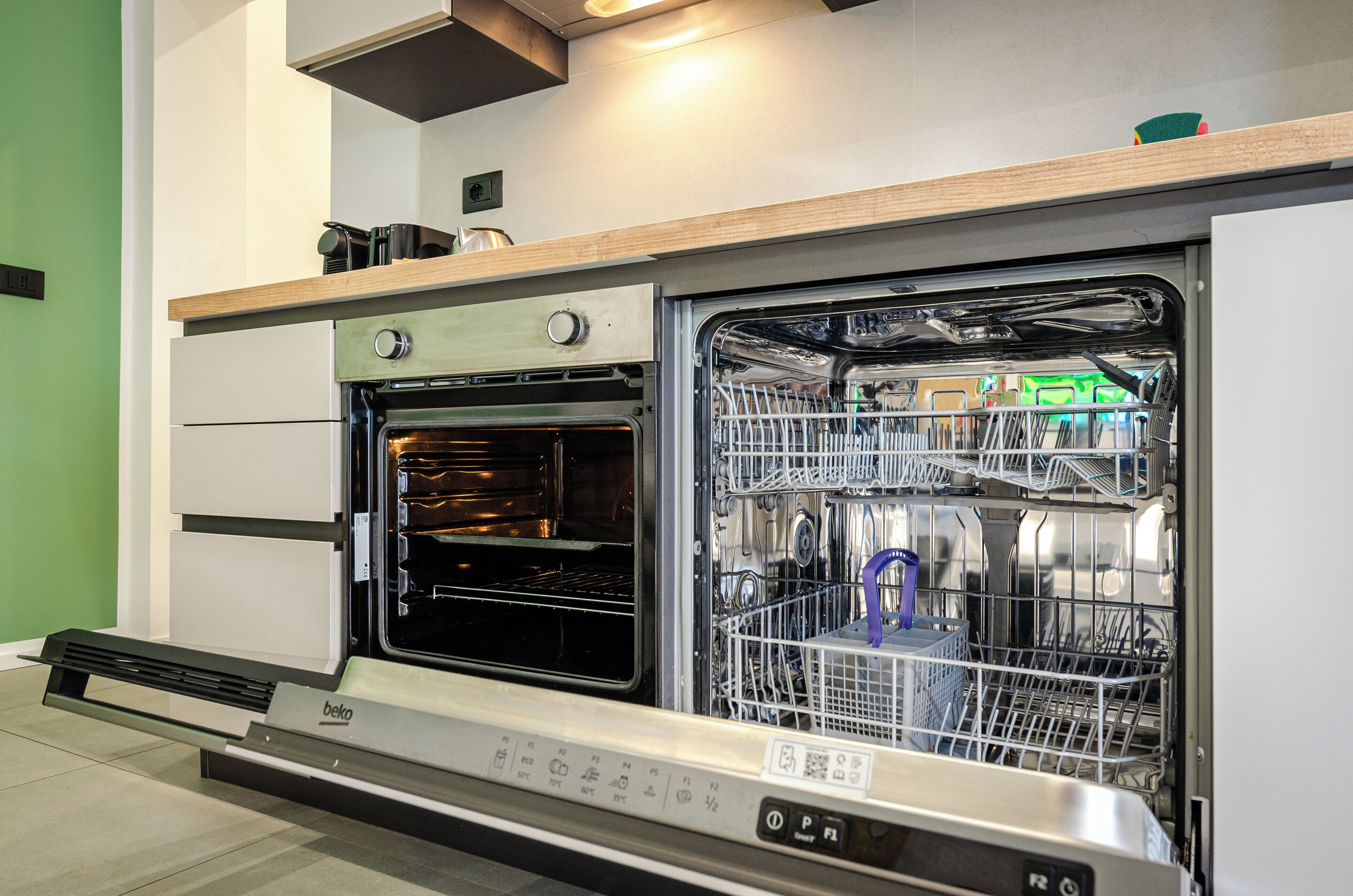 A kitchen with a built-in oven and dishwasher, a wooden countertop, and a green wall.