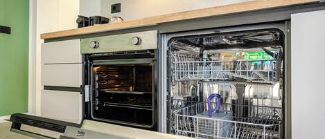 A kitchen with a built-in oven and dishwasher, a wooden countertop, and a green wall.