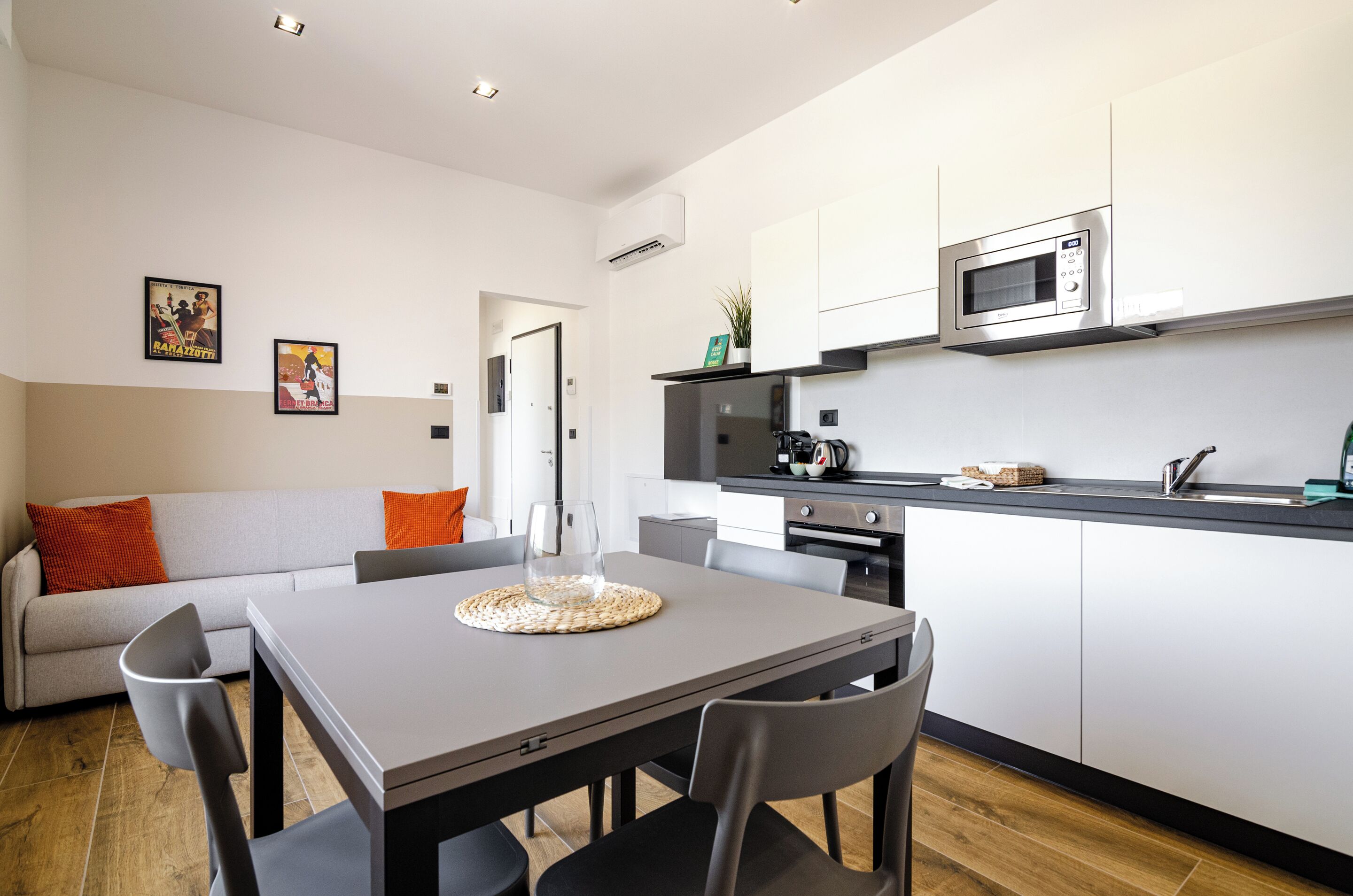 Cocina moderna con microondas, horno y pileta. Hay una mesa de comedor con sillas y un sofá con cojines naranjas.