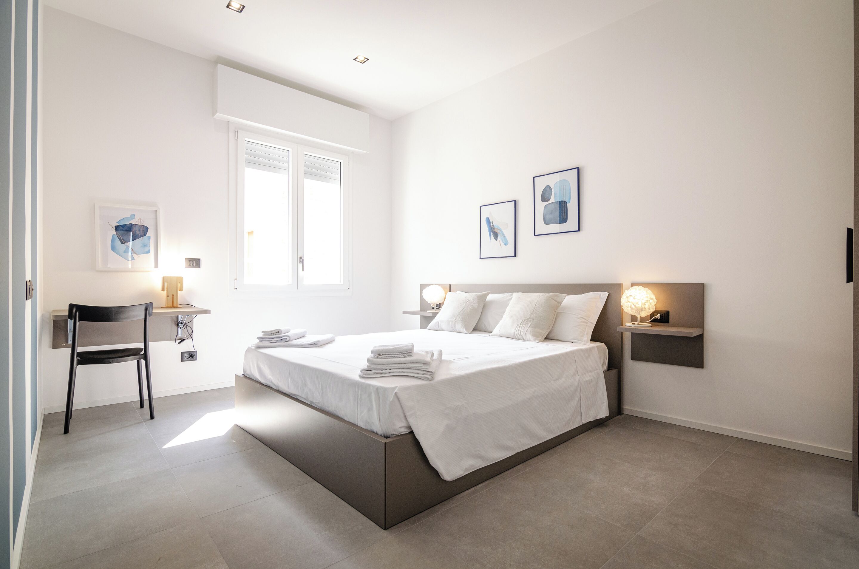 A modern bedroom with a bed, bedside tables, a chair, and artwork on the walls.