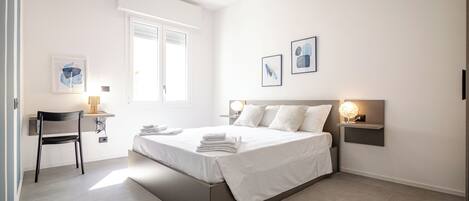 A modern bedroom with a bed, bedside tables, a chair, and artwork on the walls.