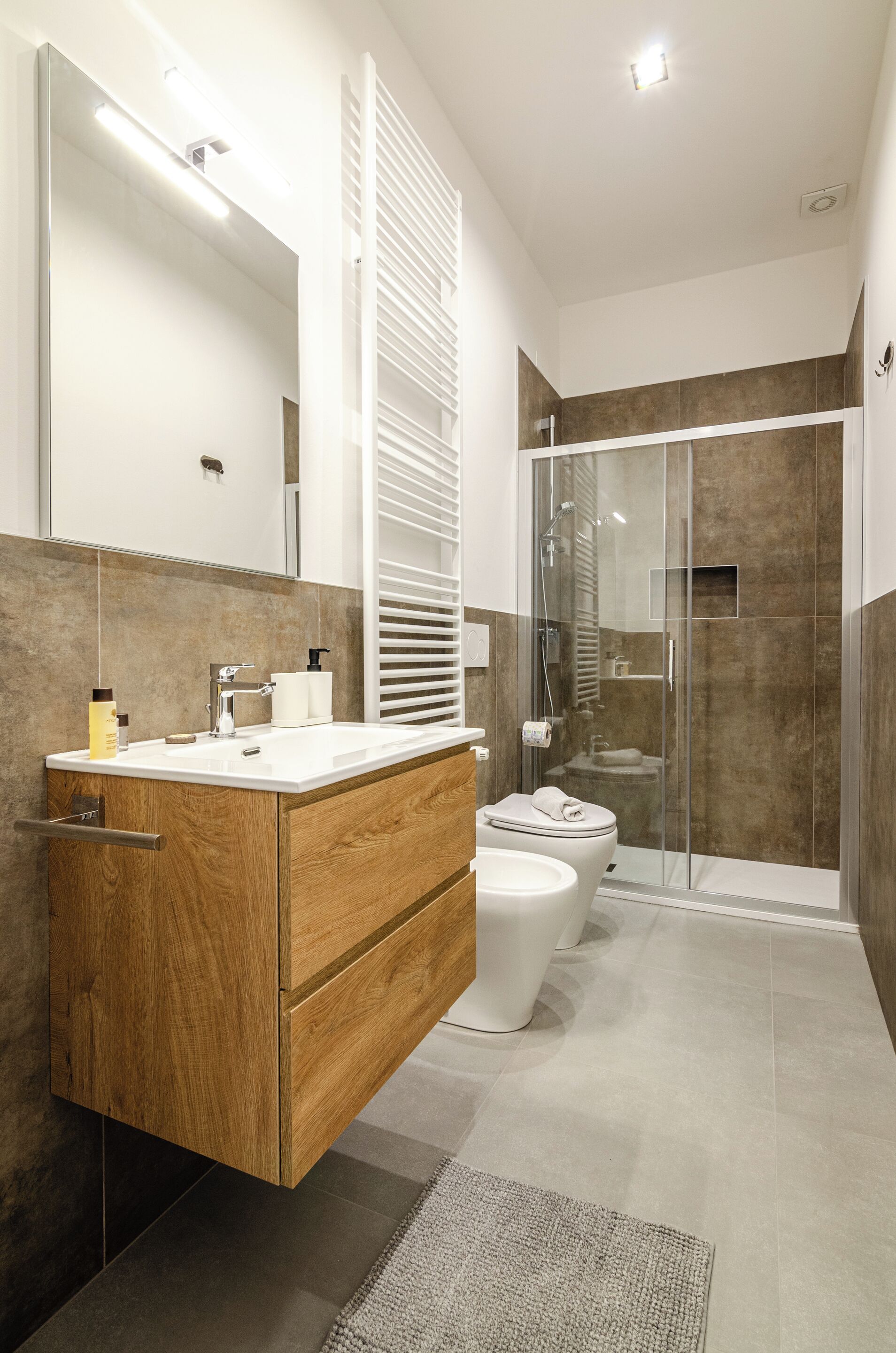 A modern bathroom with a wooden vanity, a toilet, a glass-enclosed shower, and a large mirror.